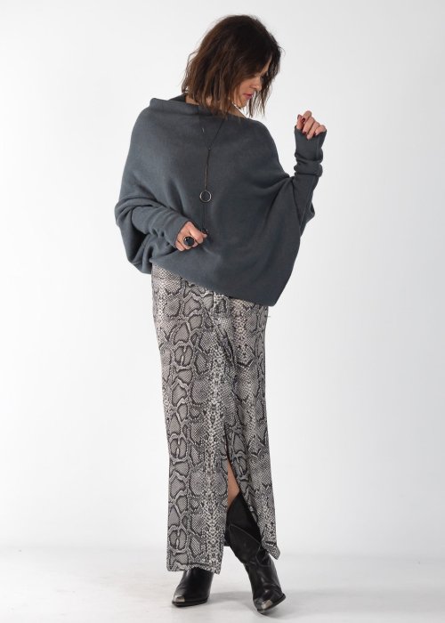 Szary sweter damski oversize o kroju nietoperzowym z dekoltem łódka i asymetrycznym dołem, stylizacja ze spodniami we wzór.