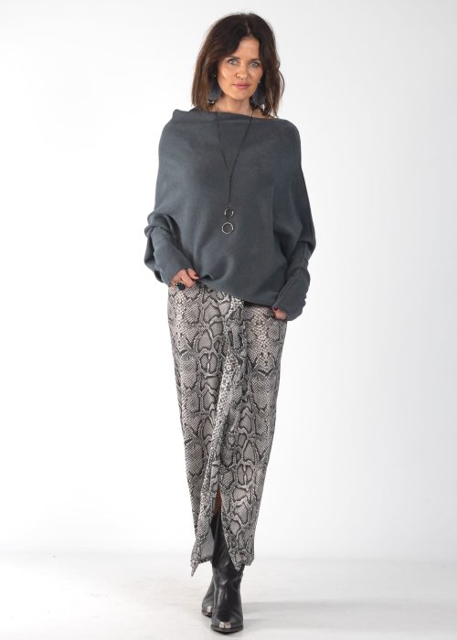 Szary sweter damski oversize o kroju nietoperzowym z dekoltem łódka i asymetrycznym dołem, stylizacja ze spodniami we wzór.