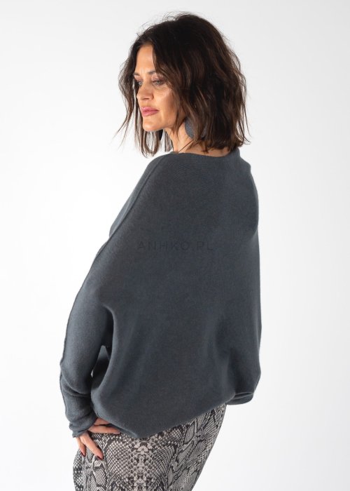 Szary sweter damski oversize o kroju nietoperzowym z dekoltem łódka i asymetrycznym dołem, stylizacja ze spodniami we wzór.