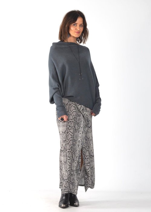 Szary sweter damski oversize o kroju nietoperzowym z dekoltem łódka i asymetrycznym dołem, stylizacja ze spodniami we wzór.