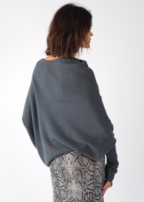 Szary sweter damski oversize o kroju nietoperzowym z dekoltem łódka i asymetrycznym dołem, stylizacja ze spodniami we wzór.