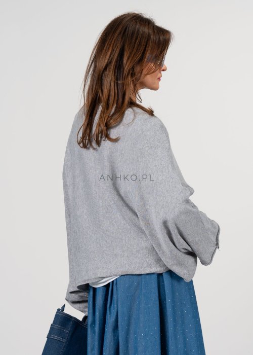 Szary sweter damski oversize z asymetrycznym dołem i szerokimi rękawami, stylizacja z niebieską spódnicą i torebką.
