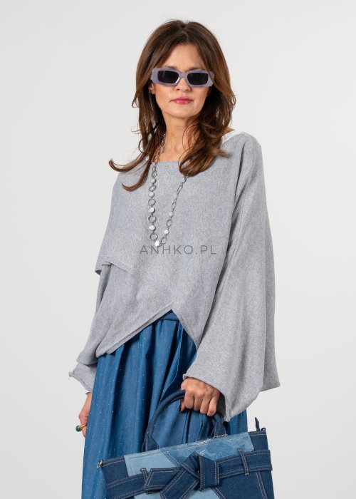 Szary sweter damski oversize z asymetrycznym dołem i szerokimi rękawami, stylizacja z niebieską spódnicą i torebką.