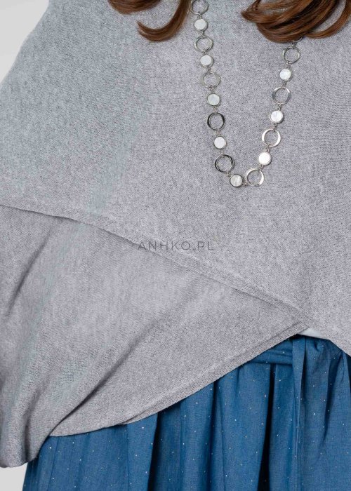 Szary sweter damski oversize z asymetrycznym dołem i szerokimi rękawami, stylizacja z niebieską spódnicą i torebką.