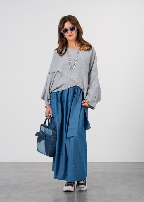 Szary sweter damski oversize z asymetrycznym dołem i szerokimi rękawami, stylizacja z niebieską spódnicą i torebką.