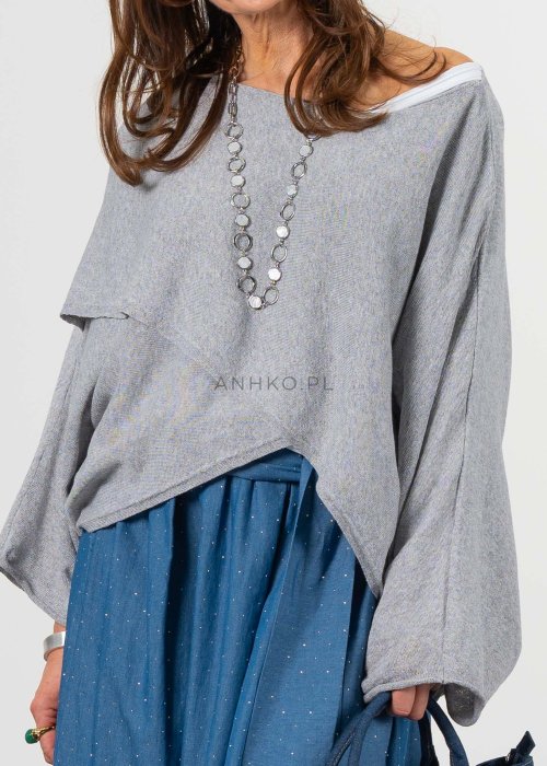 Szary sweter damski oversize z asymetrycznym dołem i szerokimi rękawami, stylizacja z niebieską spódnicą i torebką.