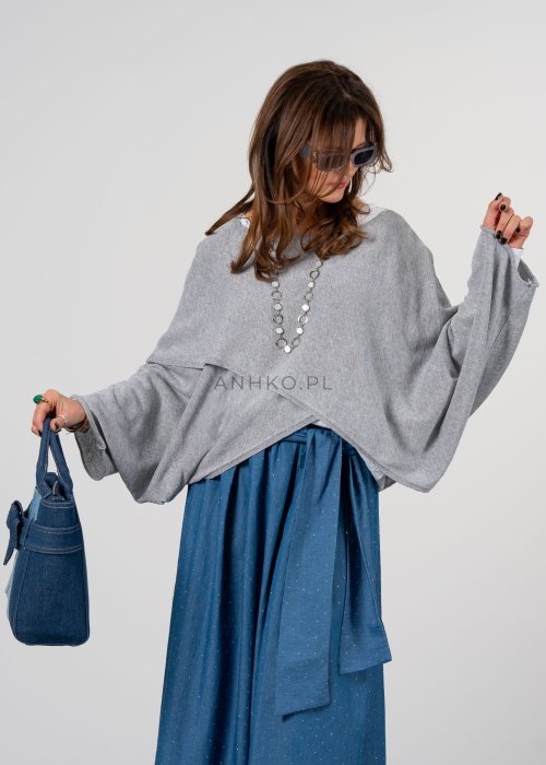Szary sweter damski oversize z asymetrycznym dołem i szerokimi rękawami, stylizacja z niebieską spódnicą i torebką.