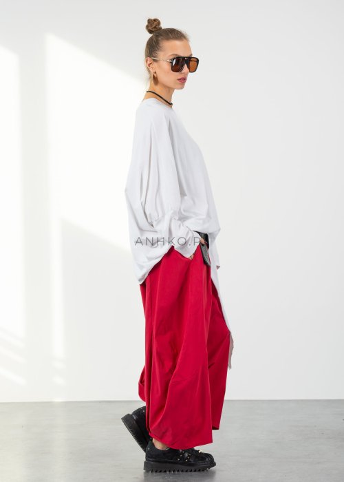 Biała bluzka oversize damska z asymetrycznym dołem i dekoltem V. Stylizacja z czerwonymi spodniami w nowoczesnym, minimalistycznym stylu.