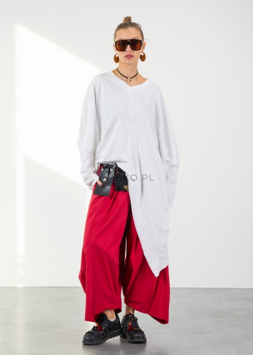 Biała bluzka oversize damska z asymetrycznym dołem i dekoltem V. Stylizacja z czerwonymi spodniami w nowoczesnym, minimalistycznym stylu.