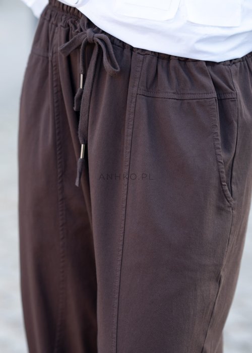 Brązowe spodnie damskie RelaxFit z elastycznym pasem i podwiniętymi nogawkami, stylizowane z białą koszulą oversize i botkami na obcasie w miejskim looku.
