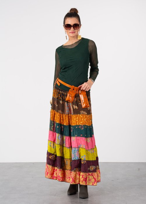 Ciemnozielona bluzka damska z transparentnymi rękawami i dekoltem łódka, elegancka stylizacja z paskiem i wzorzystą spódnicą.