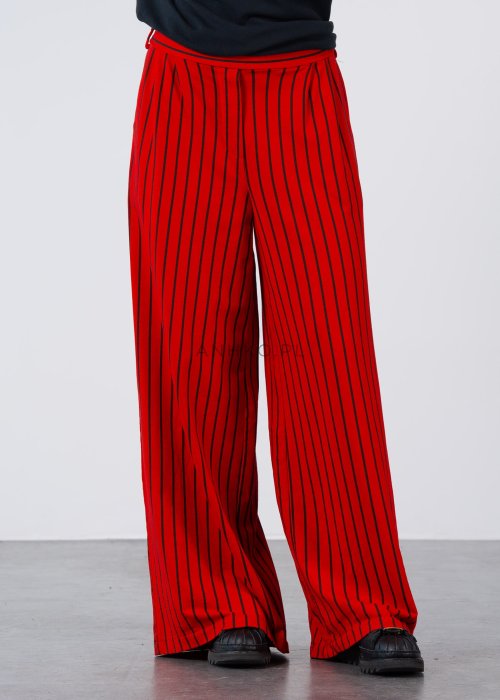 Czerwone spodnie damskie w czarne pionowe paski o szerokim kroju, zestawione z czarną bluzą i botkami na obcasie w nowoczesnej stylizacji.