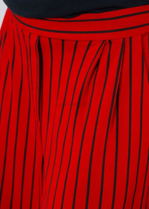 Czerwone spodnie damskie w czarne pionowe paski o szerokim kroju, zestawione z czarną bluzą i botkami na obcasie w nowoczesnej stylizacji.