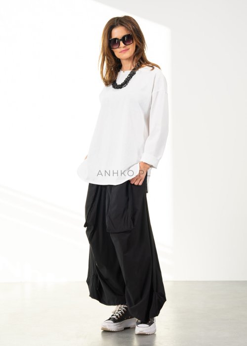 Damskie czarne spodnie parachute o szerokim kroju z dużymi kieszeniami i gumką w pasie, zestawione ze sneakersami. Model o luźnej, objętościowej formie.