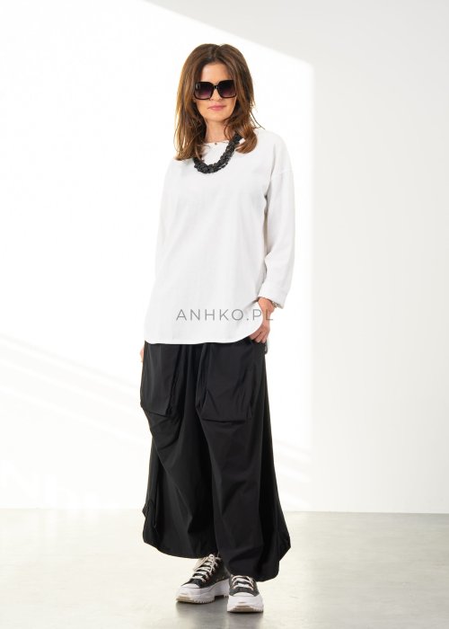 Damskie czarne spodnie parachute o szerokim kroju z dużymi kieszeniami i gumką w pasie, zestawione ze sneakersami. Model o luźnej, objętościowej formie.