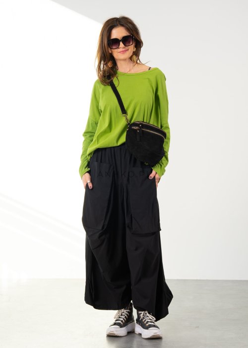 Damskie czarne spodnie parachute o szerokim kroju z dużymi kieszeniami i gumką w pasie, zestawione ze sneakersami. Model o luźnej, objętościowej formie.