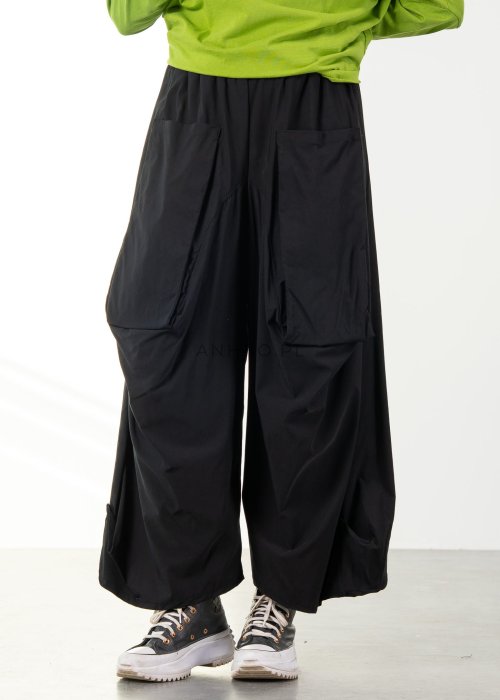 Damskie czarne spodnie parachute o szerokim kroju z dużymi kieszeniami i gumką w pasie, zestawione ze sneakersami. Model o luźnej, objętościowej formie.