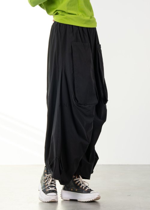 Damskie czarne spodnie parachute o szerokim kroju z dużymi kieszeniami i gumką w pasie, zestawione ze sneakersami. Model o luźnej, objętościowej formie.