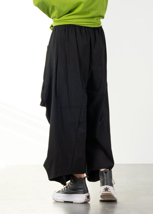 Damskie czarne spodnie parachute o szerokim kroju z dużymi kieszeniami i gumką w pasie, zestawione ze sneakersami. Model o luźnej, objętościowej formie.