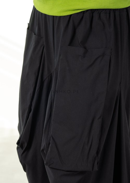 Damskie czarne spodnie parachute o szerokim kroju z dużymi kieszeniami i gumką w pasie, zestawione ze sneakersami. Model o luźnej, objętościowej formie.