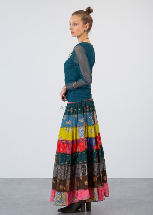 Morska bluzka damska z transparentnymi rękawami i dekoltem łódka, elegancka stylizacja z biżuterią i wzorzystą spódnicą.