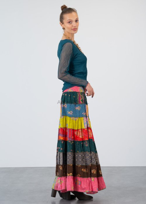 Morska bluzka damska z transparentnymi rękawami i dekoltem łódka, elegancka stylizacja z biżuterią i wzorzystą spódnicą.