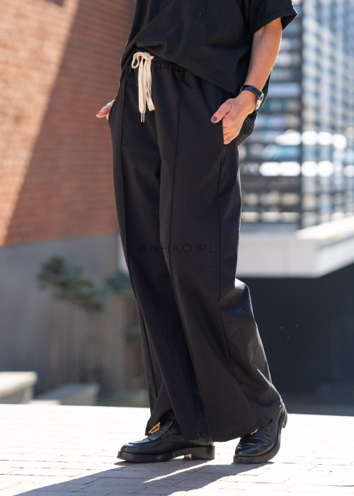 Czarne spodnie dresowe damskie z szeroką nogawką i elastyczną talią z troczkiem, stylizacja miejska