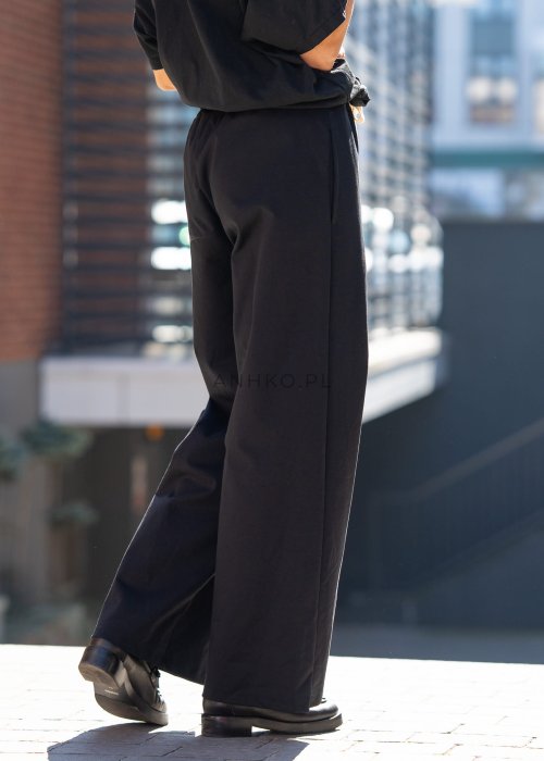 Czarne spodnie dresowe damskie z szeroką nogawką i elastyczną talią z troczkiem, stylizacja miejska