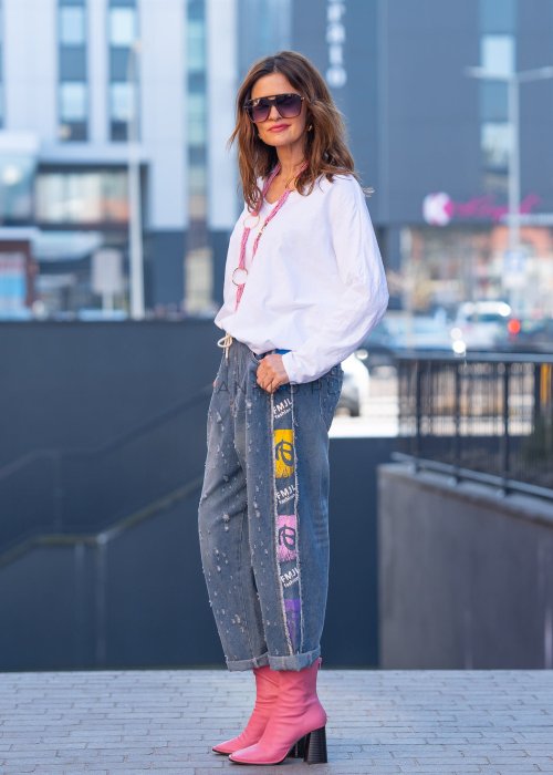 Biała bluzka damska oversize z długim rękawem i dekoltem V w stylizacji z jeansami i różowym naszyjnikiem.