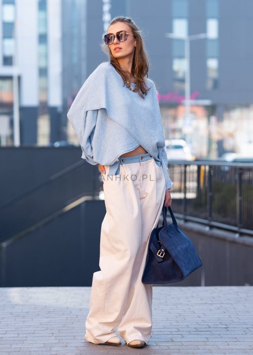 Jasnoniebieski sweter oversize z asymetrycznym dołem, stylizowany z jasnymi szerokimi spodniami i granatową torebką w miejskim looku.