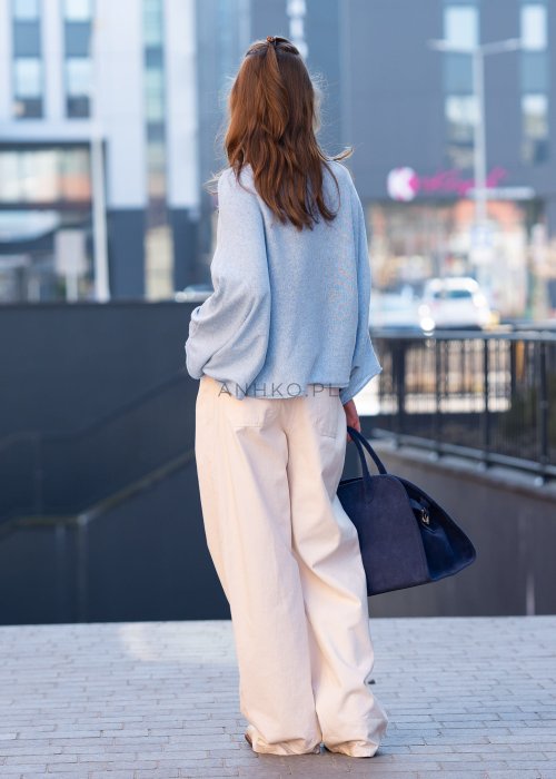 Jasnoniebieski sweter oversize z asymetrycznym dołem, stylizowany z jasnymi szerokimi spodniami i granatową torebką w miejskim looku.