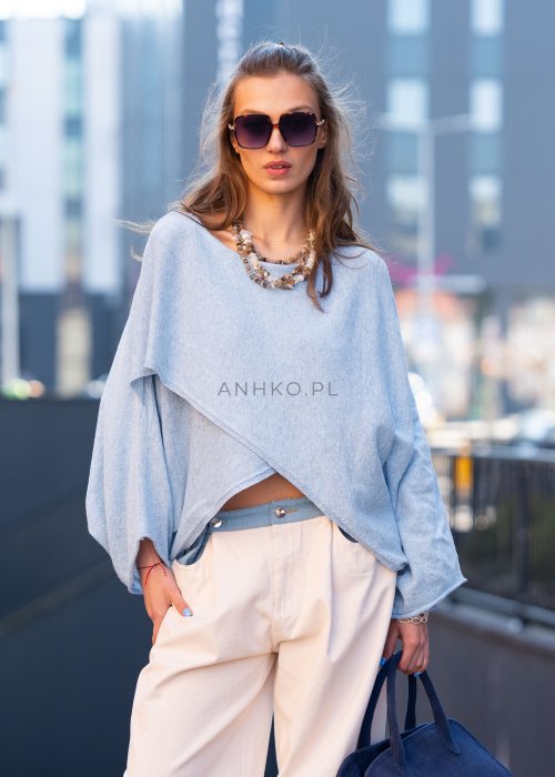 Jasnoniebieski sweter oversize z asymetrycznym dołem, stylizowany z jasnymi szerokimi spodniami i granatową torebką w miejskim looku.