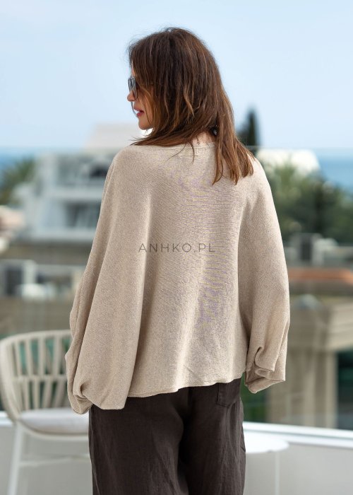 Kremowy sweter oversize z asymetrycznym dołem i szerokimi rękawami, zestawiony z brązowymi spodniami o luźnym kroju. Stylizacja w klimacie casual premium z botkami na obcasie.