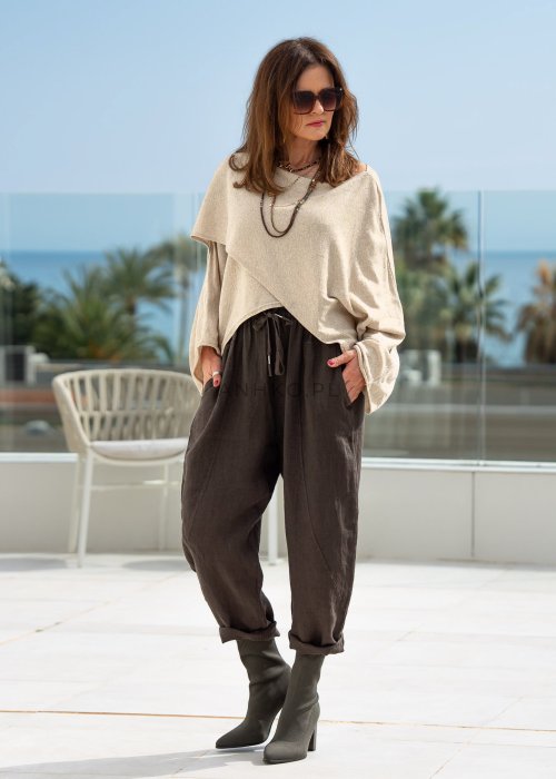Kremowy sweter oversize z asymetrycznym dołem i szerokimi rękawami, zestawiony z brązowymi spodniami o luźnym kroju. Stylizacja w klimacie casual premium z botkami na obcasie.