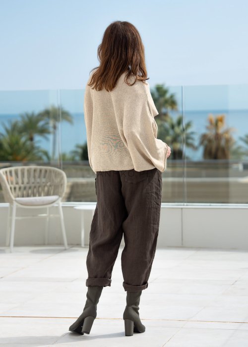 Kremowy sweter oversize z asymetrycznym dołem i szerokimi rękawami, zestawiony z brązowymi spodniami o luźnym kroju. Stylizacja w klimacie casual premium z botkami na obcasie.