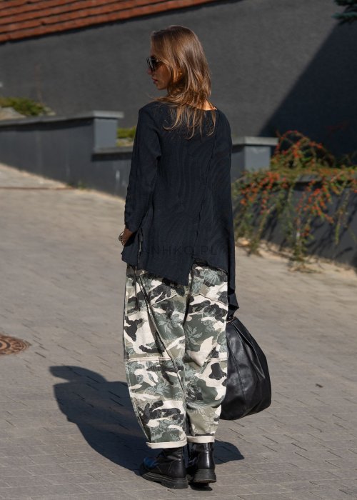 Damskie spodnie dresowe w print moro z motywem roślinnym, o luźnym kroju z kieszeniami i przeszyciami. Stylizacja z podwiniętymi nogawkami i czarnymi botkami.