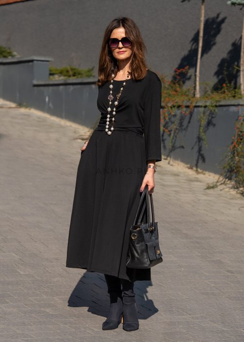 Czarna sukienka midi z wiązaniem w talii i rękawem 3/4, o lekko rozkloszowanym kroju. Stylizacja z botkami i torebką w eleganckim, miejskim wydaniu.