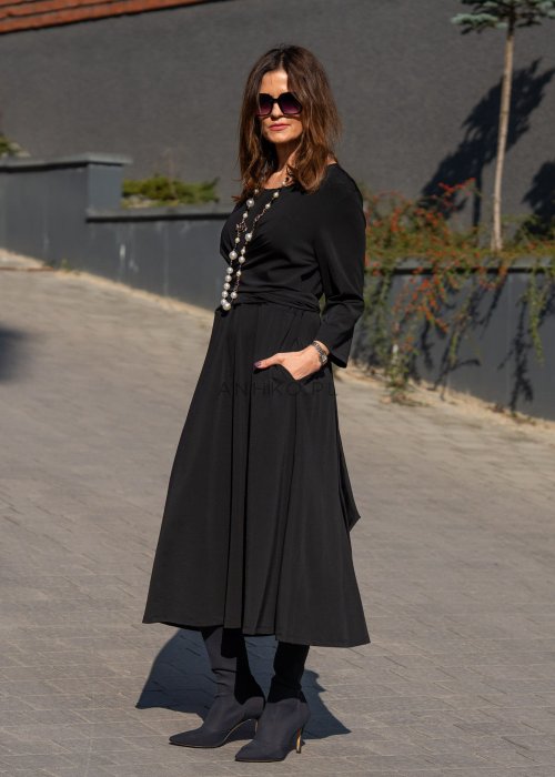 Czarna sukienka midi z wiązaniem w talii i rękawem 3/4, o lekko rozkloszowanym kroju. Stylizacja z botkami i torebką w eleganckim, miejskim wydaniu.