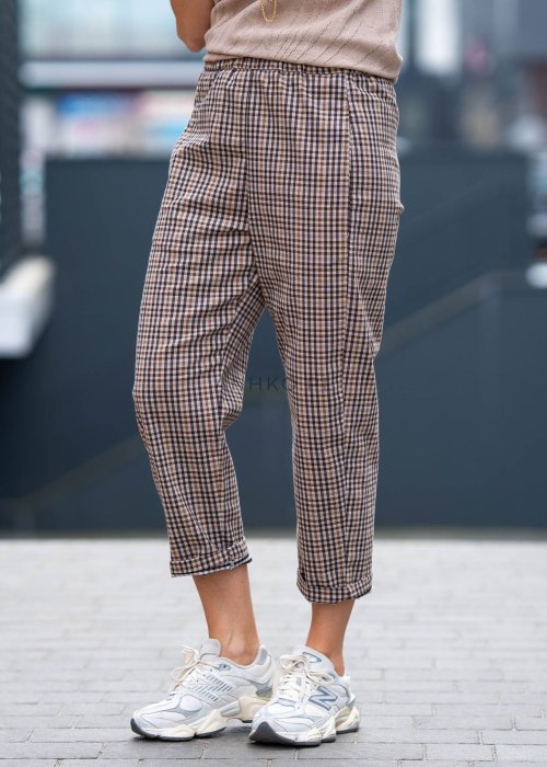 Beżowo-brązowe spodnie damskie w drobną kratę o długości 7/8 z elastyczną talią i kieszeniami, zestawione ze sneakersami w miejskiej stylizacji.