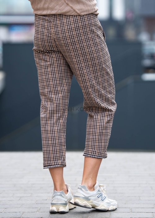 Beżowo-brązowe spodnie damskie w drobną kratę o długości 7/8 z elastyczną talią i kieszeniami, zestawione ze sneakersami w miejskiej stylizacji.