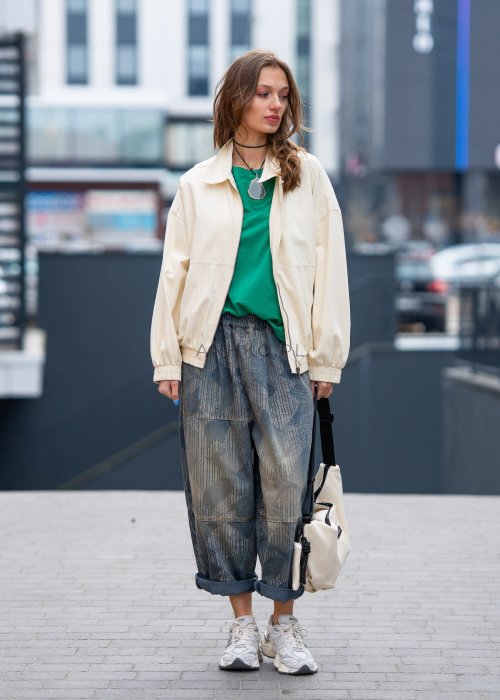 Zielona bluzka oversize z szerokim dekoltem i krótkim rękawem, zestawiona z luźnymi spodniami w casualowej, miejskiej stylizacji.