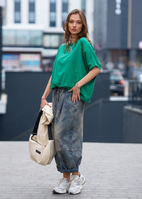 Zielona bluzka oversize z szerokim dekoltem i krótkim rękawem, zestawiona z luźnymi spodniami w casualowej, miejskiej stylizacji.