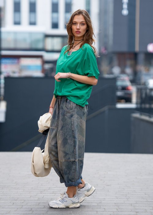 Zielona bluzka oversize z szerokim dekoltem i krótkim rękawem, zestawiona z luźnymi spodniami w casualowej, miejskiej stylizacji.