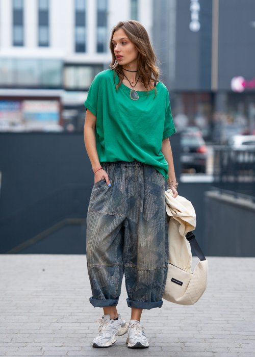 Zielona bluzka oversize z szerokim dekoltem i krótkim rękawem, zestawiona z luźnymi spodniami w casualowej, miejskiej stylizacji.