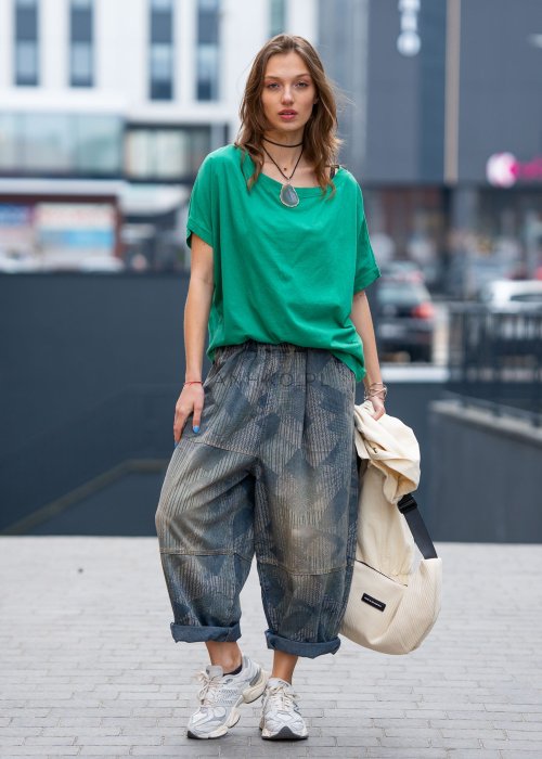 Zielona bluzka oversize z szerokim dekoltem i krótkim rękawem, zestawiona z luźnymi spodniami w casualowej, miejskiej stylizacji.