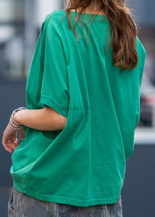 Zielona bluzka oversize z szerokim dekoltem i krótkim rękawem, zestawiona z luźnymi spodniami w casualowej, miejskiej stylizacji.