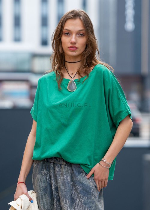 Zielona bluzka oversize z szerokim dekoltem i krótkim rękawem, zestawiona z luźnymi spodniami w casualowej, miejskiej stylizacji.