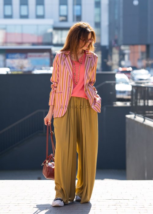 Musztardowe spodnie damskie z szeroką, lejącą nogawką i elastycznym pasem, stylizowane z białym t-shirtem w casualowym, miejskim stylu.