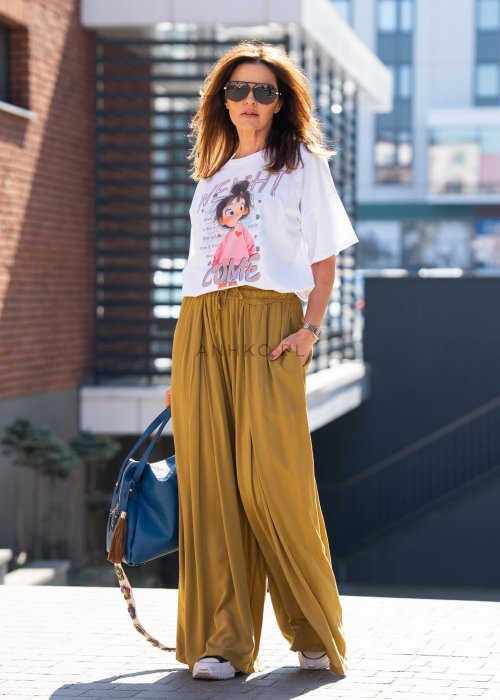 Musztardowe spodnie damskie z szeroką, lejącą nogawką i elastycznym pasem, stylizowane z białym t-shirtem w casualowym, miejskim stylu.