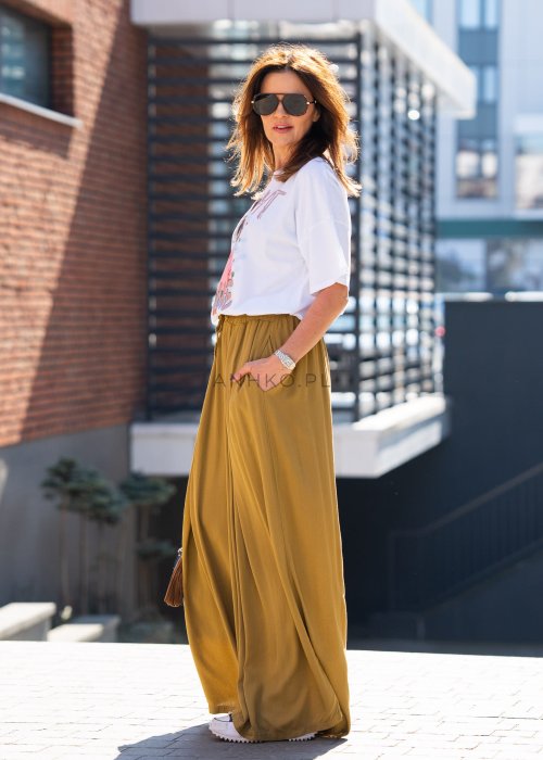 Musztardowe spodnie damskie z szeroką, lejącą nogawką i elastycznym pasem, stylizowane z białym t-shirtem w casualowym, miejskim stylu.